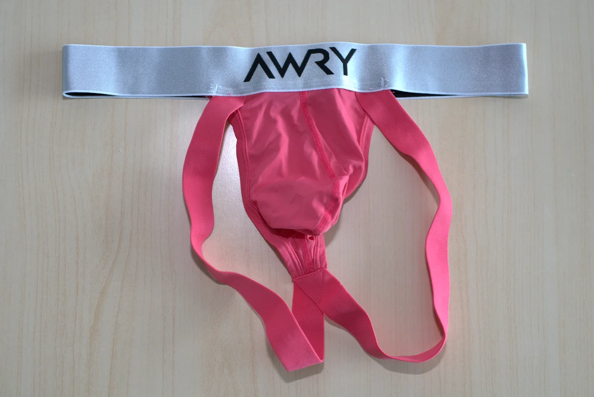 Front flat lay of the pink AWRY APEX Jock Thong with its silver waistband and straps extended.