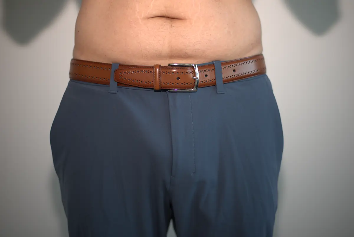 Wide front view of blue-gray dress pants worn over the AWRY RIBBED Thong with a tucked-in shirt, belt, and surrounding neutral wall.