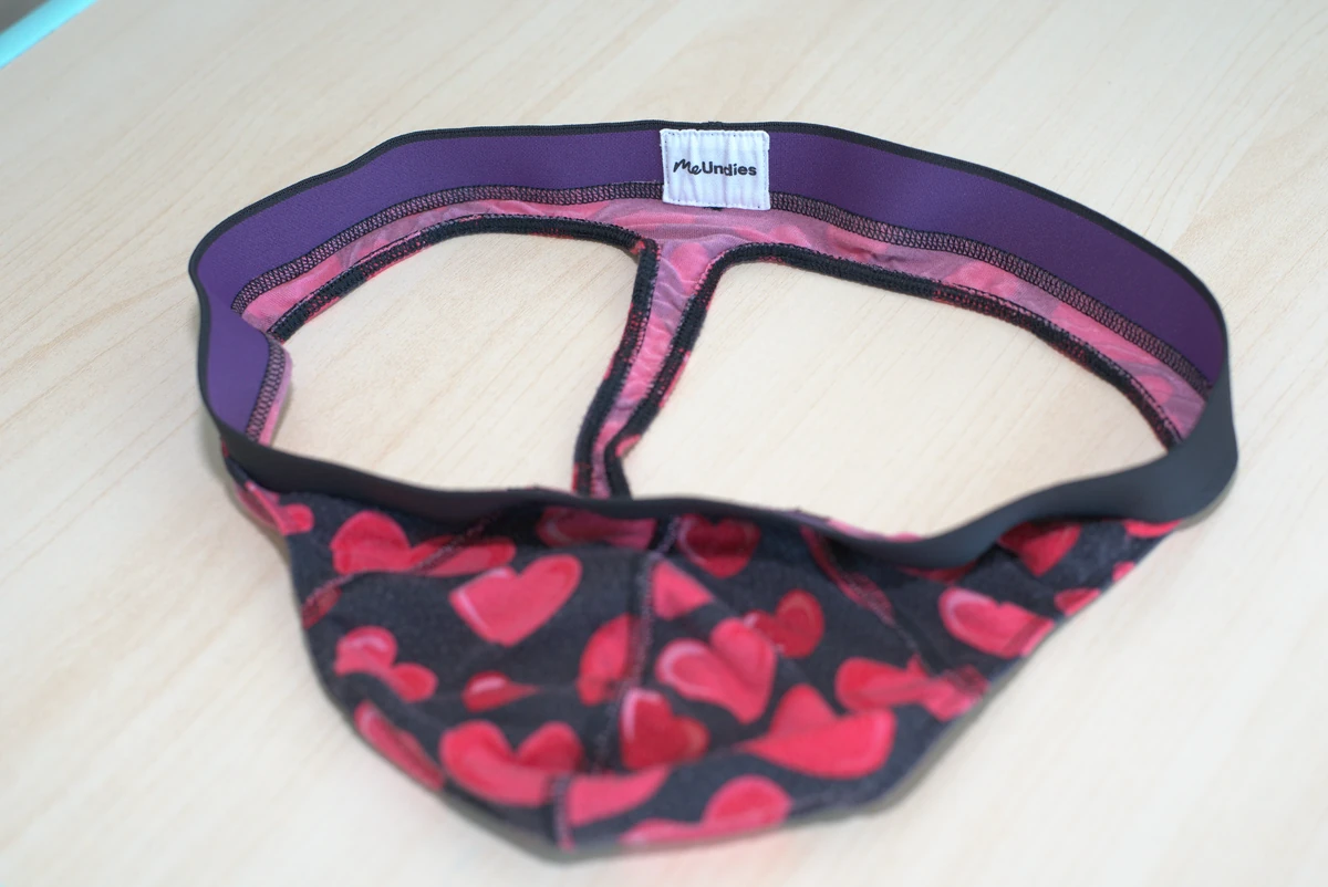 Open MeUndies Pouch Front Thong on a wood surface, showing the waistband, rear strap attachment and front panel construction.