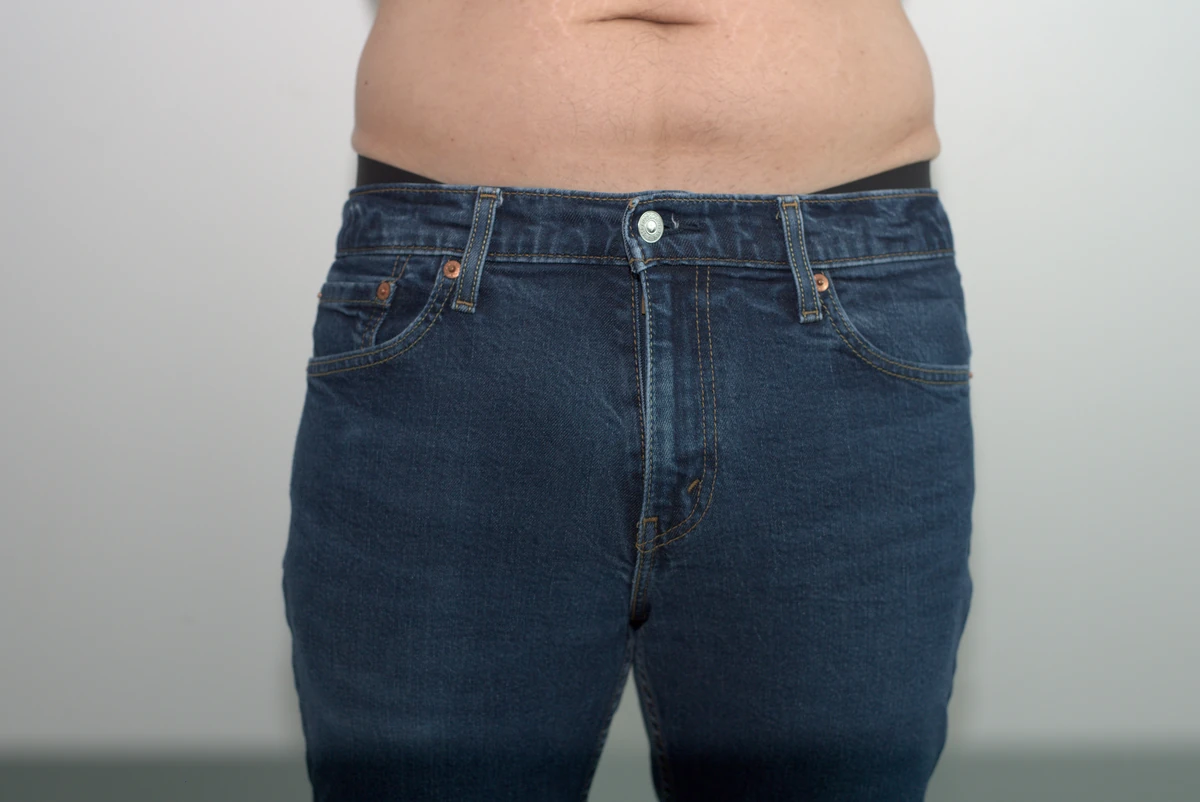 Full front view of jeans worn over the MeUndies Pouch Front Thong, with both sides of the jeans and surrounding wall visible.