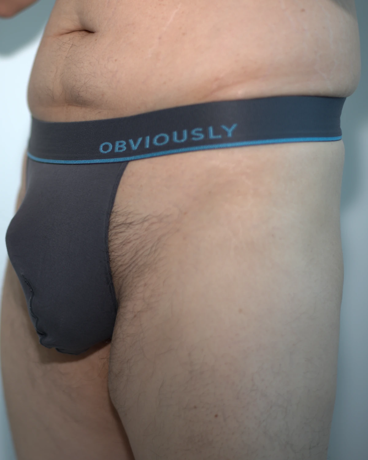 Front three-quarter view of the Titanium Obviously Primeman Thong in Medium, showing its natural pouch drape, waistband position, and upper thigh.