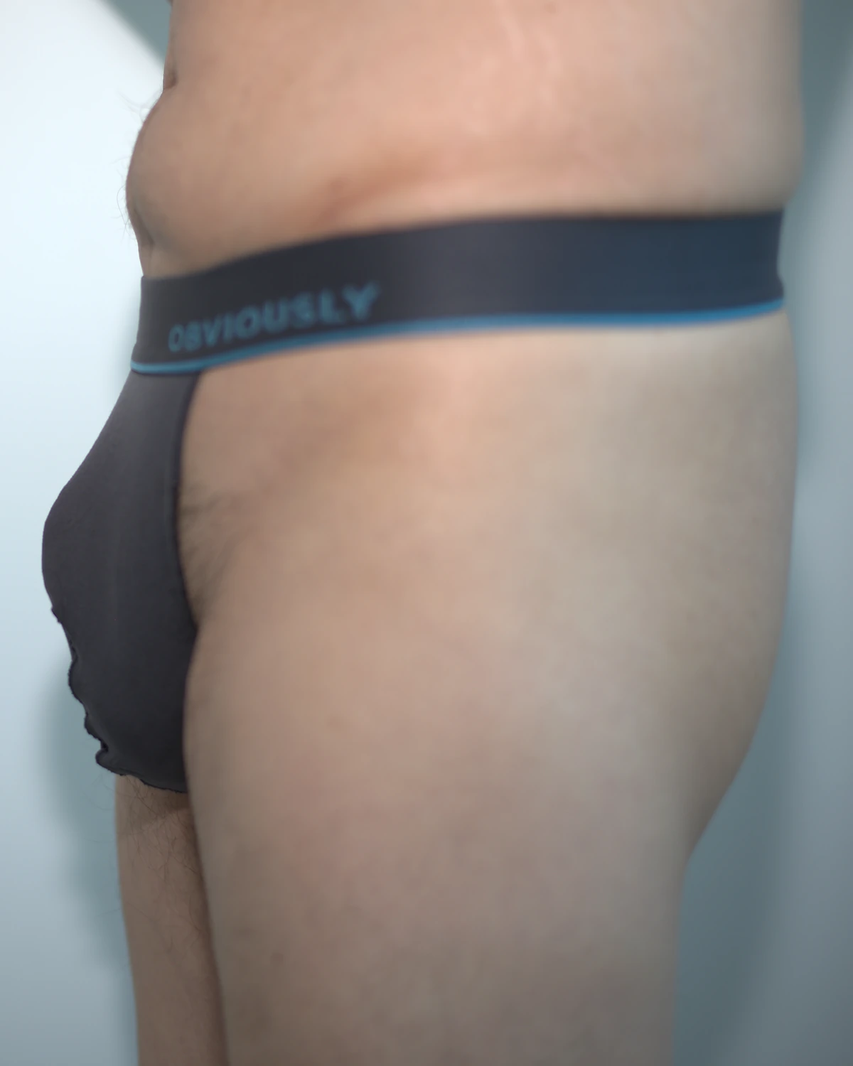 Side view of the Titanium Obviously Primeman Thong in Medium, showing its low pouch projection, waistband level, and upper thigh.